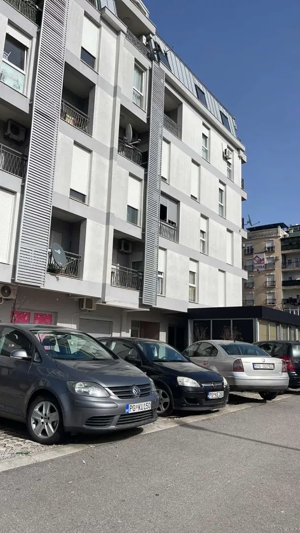 Svijetla fasada moderne stambene zgrade sa parkingom ispred.