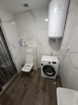 Small bathroom with a walk-in shower, toilet, washing machine, and water heater. - image 14
