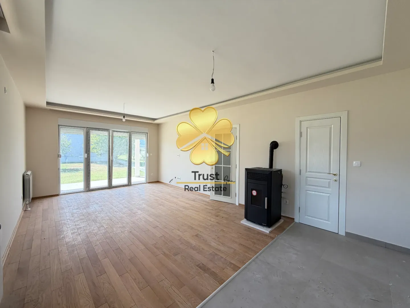 Empty living room with wooden flooring, pellet stove, and access to the yard.