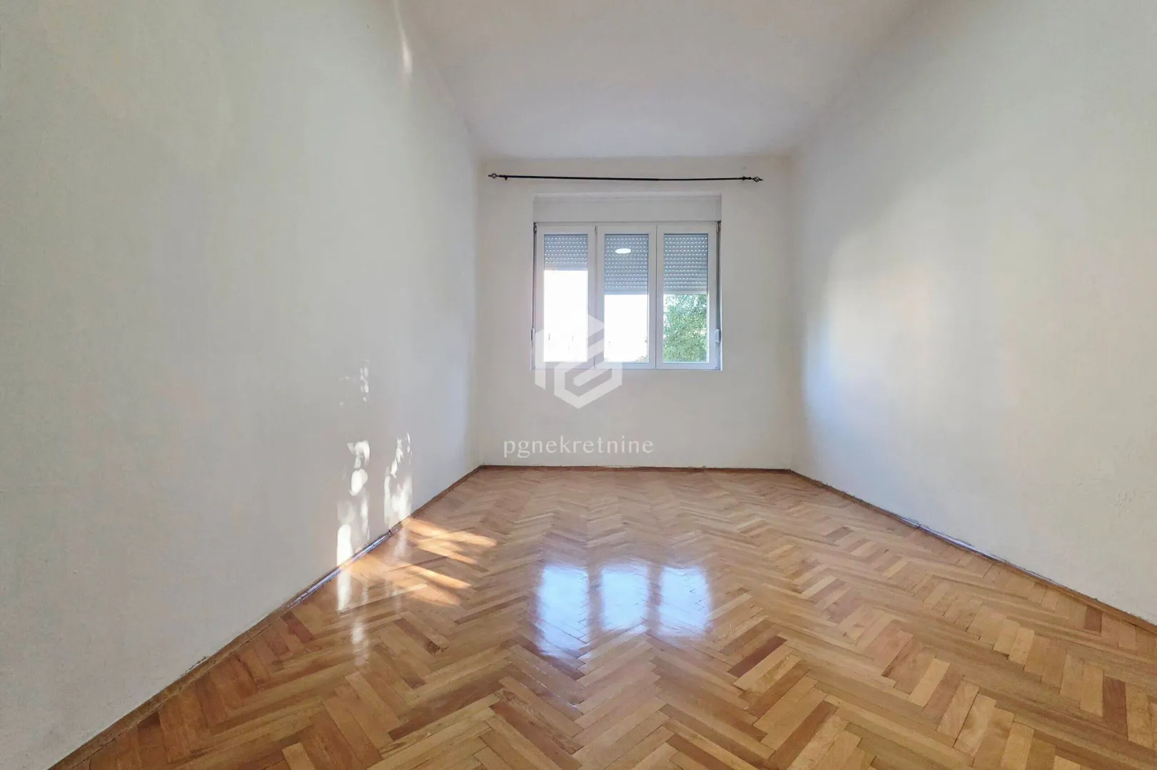 Empty room with parquet flooring and a window.
