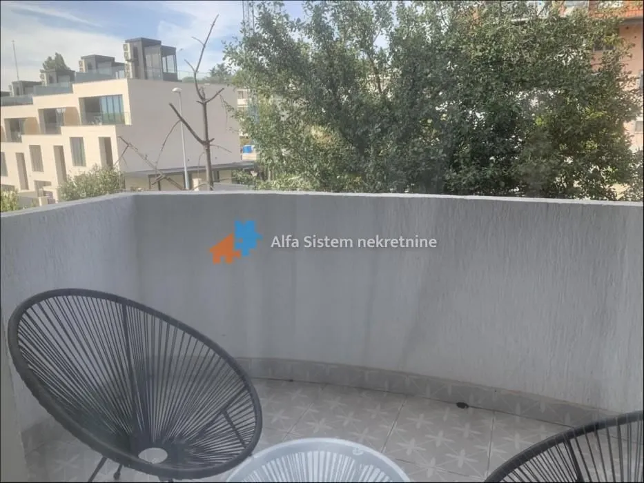 Manji balkon sa stolicama i pogledom na naselje i zelenilo.