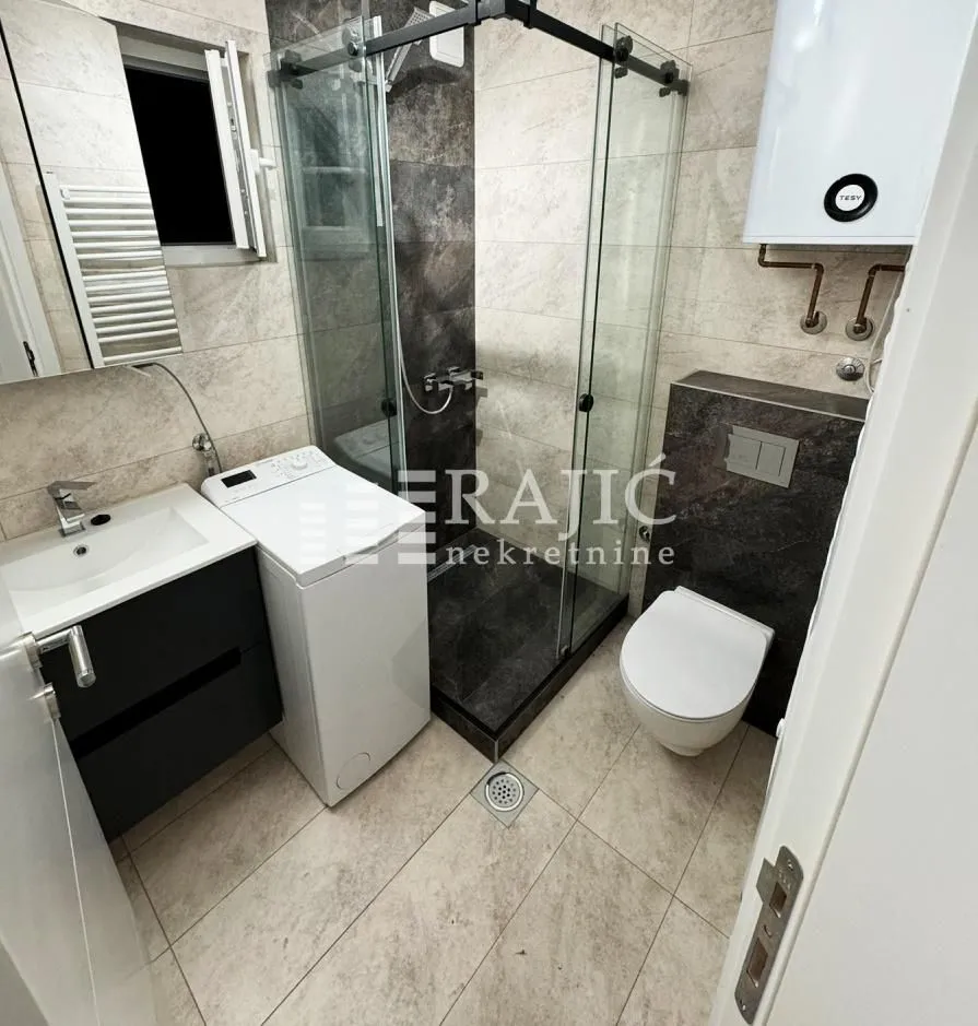 Modernly equipped bathroom with a shower cabin, sink, and toilet bowl.