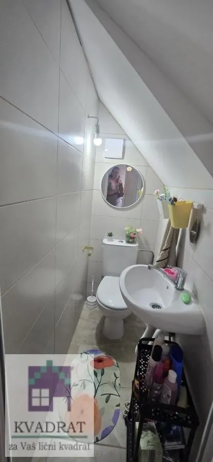 Manje kupatilo sa lavaboom, wc šoljom i ogledalom pod kosim krovom.