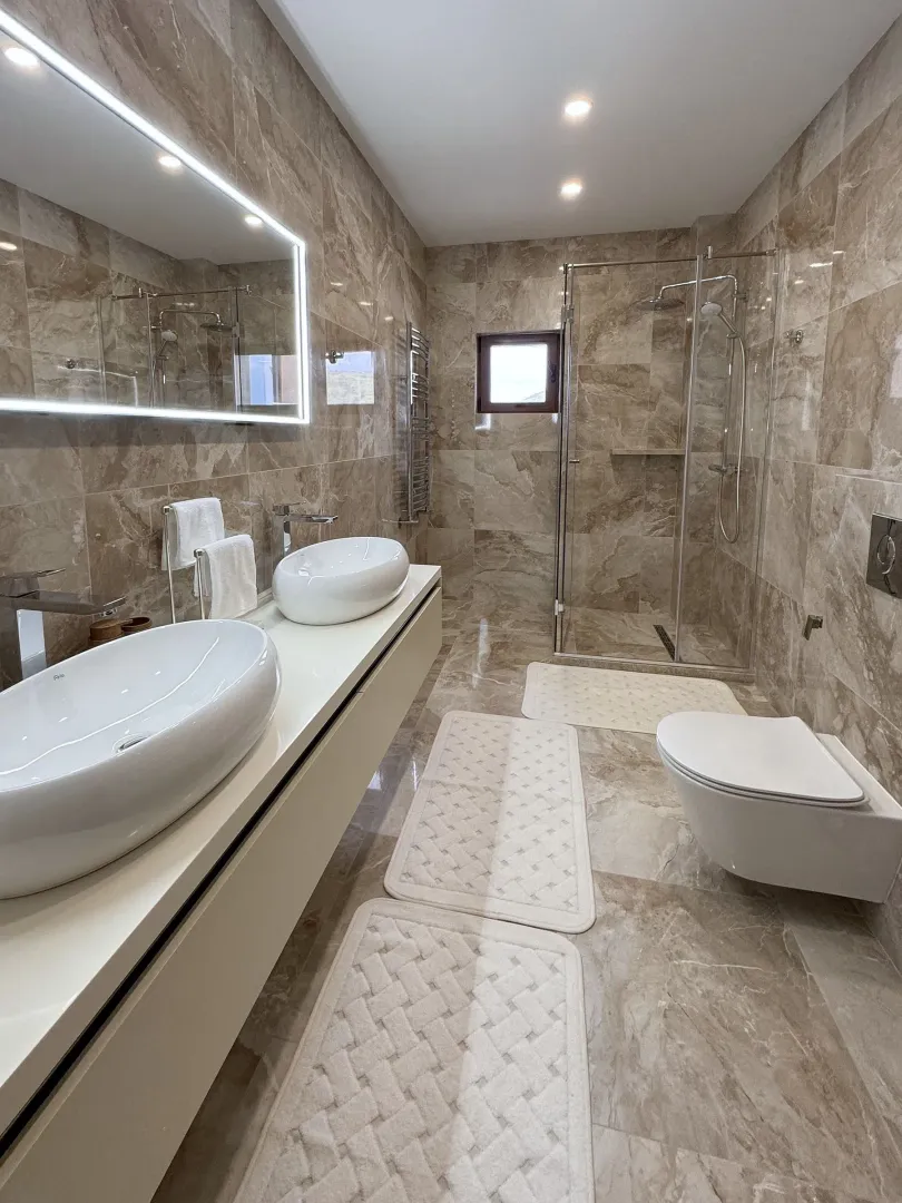 Modern bathroom with double sinks, walk-in shower, and wall-hung toilet.
