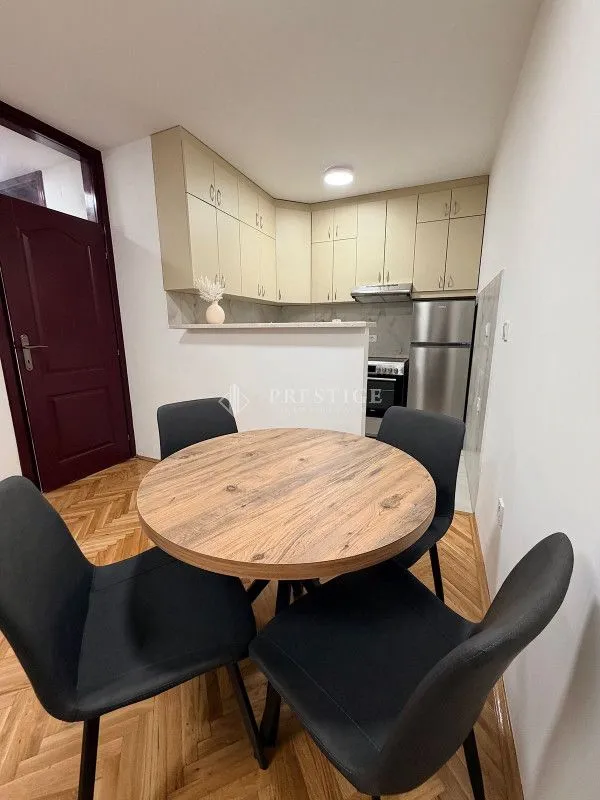 Dining area with a table and black chairs and a view of the kitchen.