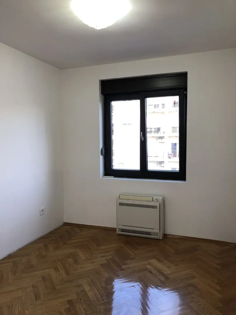 An empty room with parquet flooring and a window.
