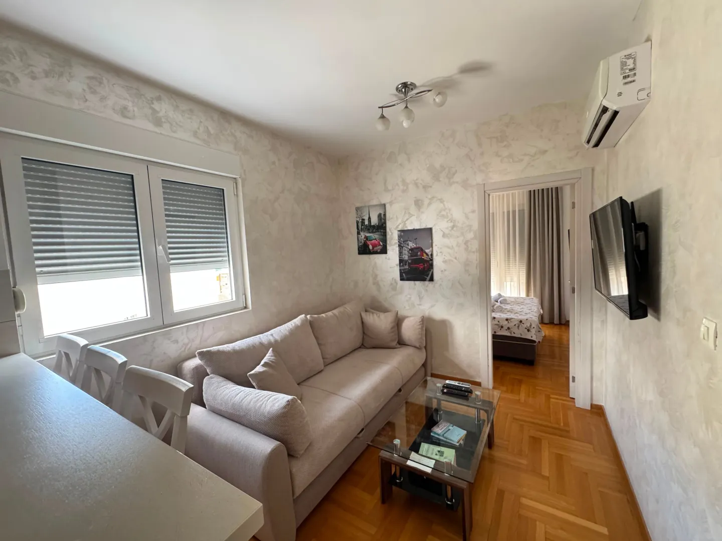 A bright living room featuring a sofa, a glass coffee table, and a doorway leading to a bedroom.