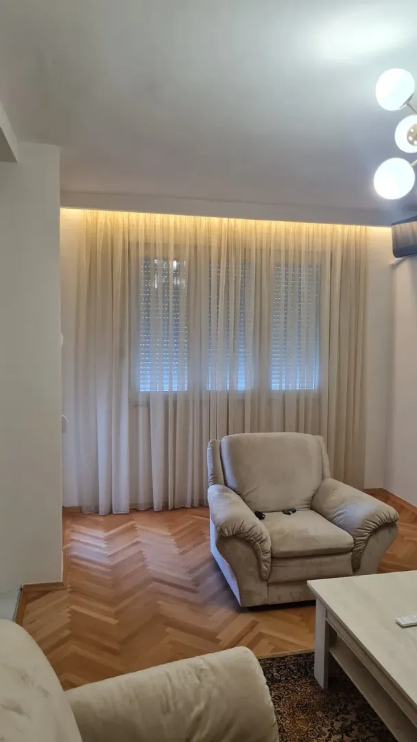 Svijetla dnevna soba sa udobnom foteljom i parketom.