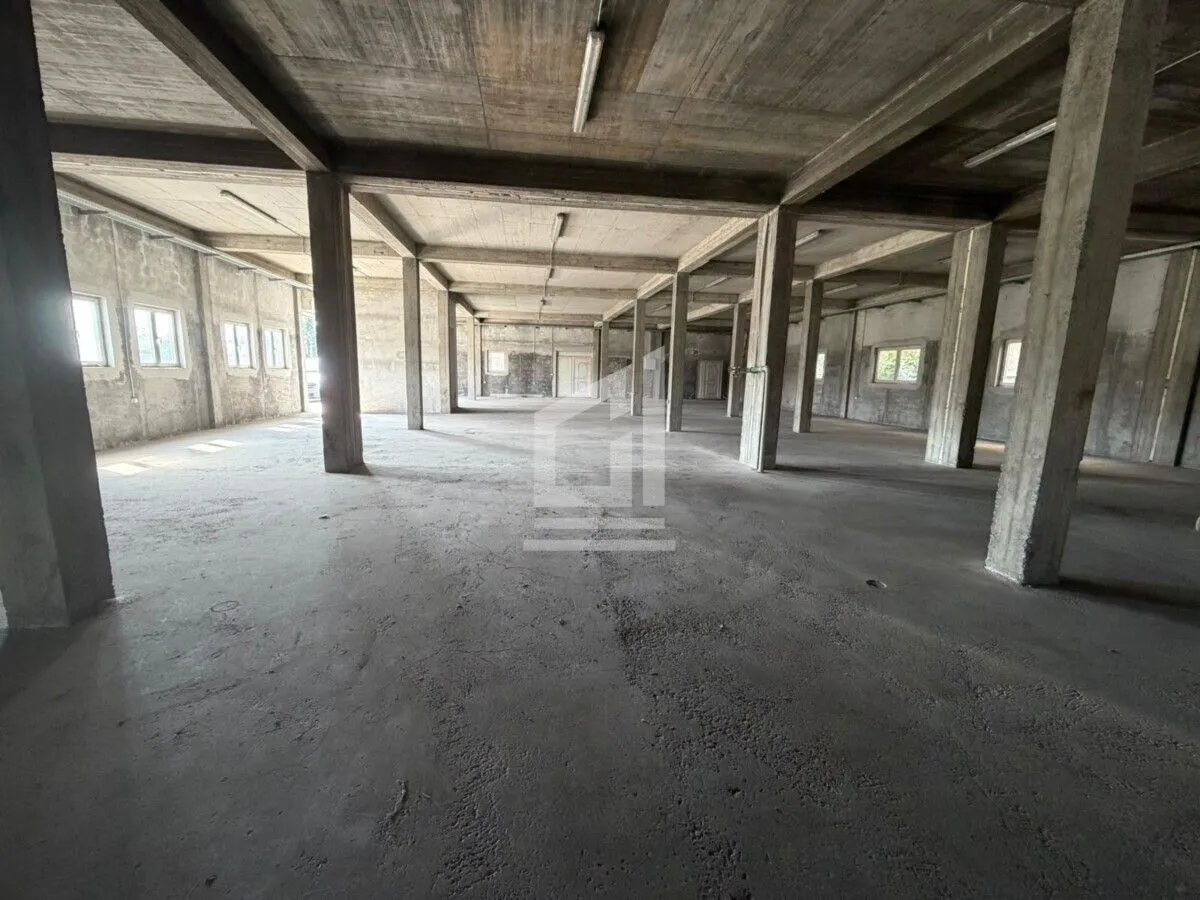 Large unfurnished space in grey phase with concrete pillars and beams.