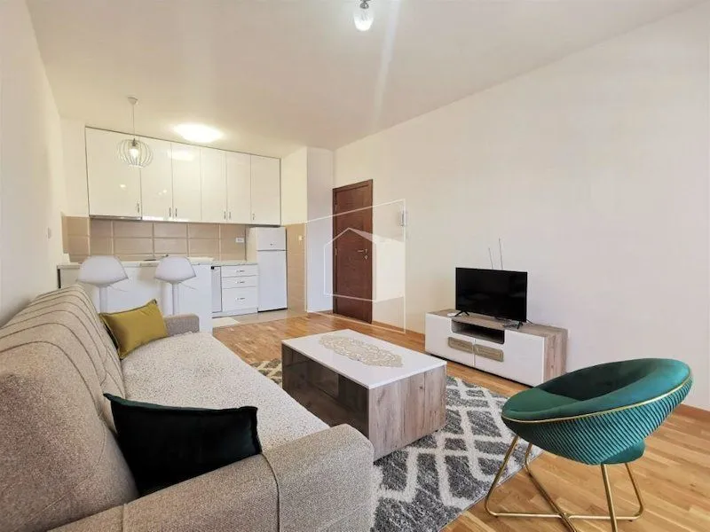 Living room with a sofa, TV, and kitchen in the background.