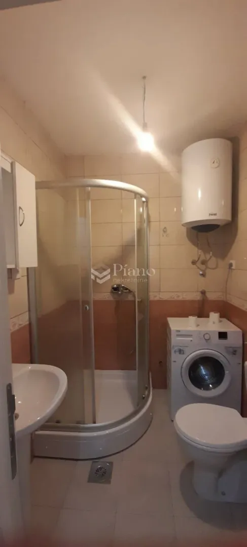 Kupatilo opremljeno tuš kabinom, umivaonikom, wc šoljom i mašinom za veš.