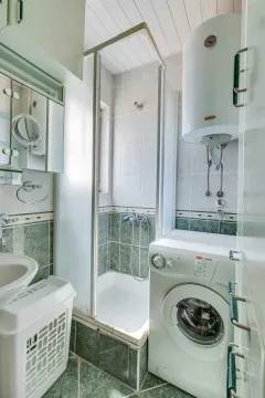 Small bathroom with a shower cabin, sink, and washing machine. - image 16