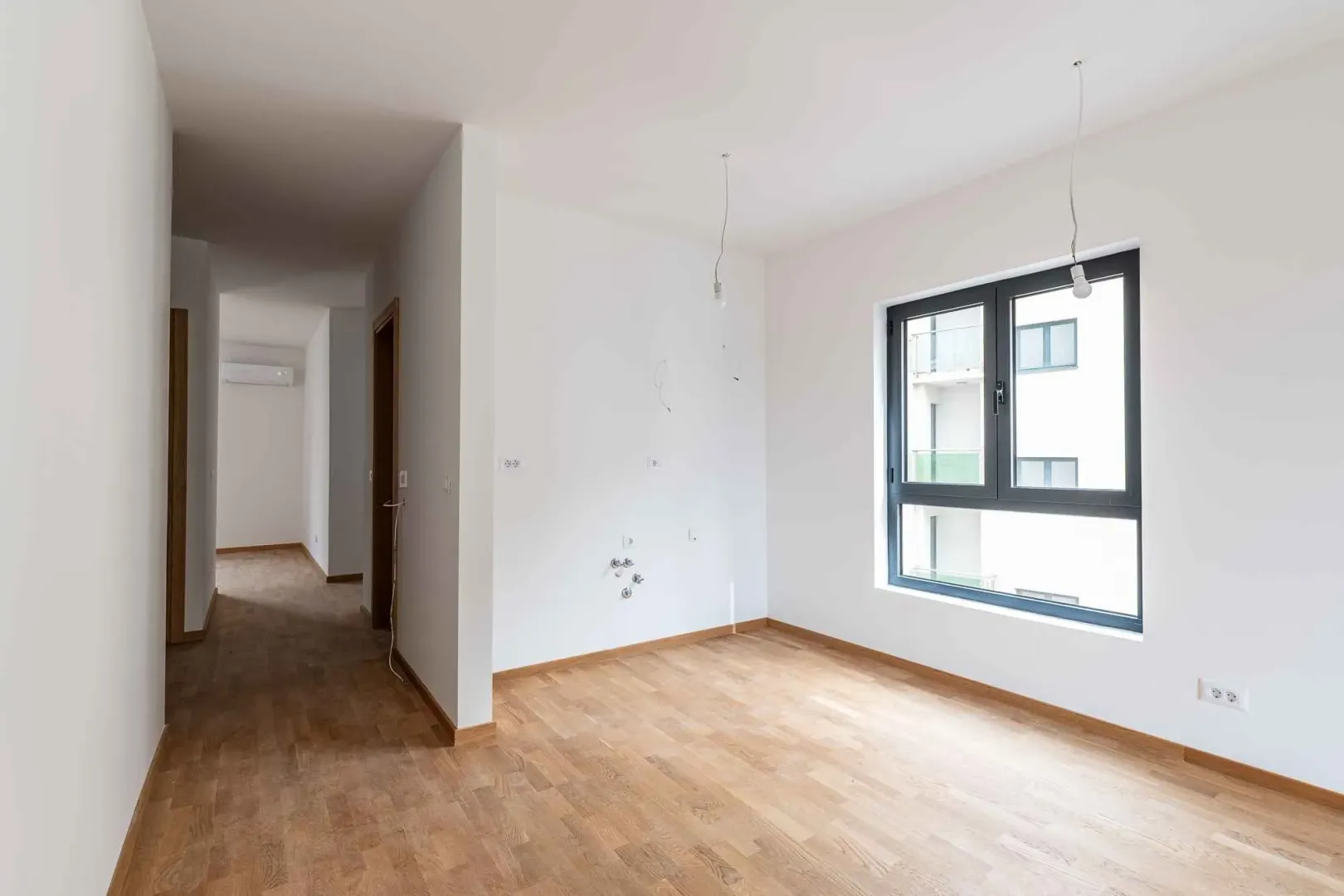 Prazna neopremljena soba sa drvenim podom i prozorom.
