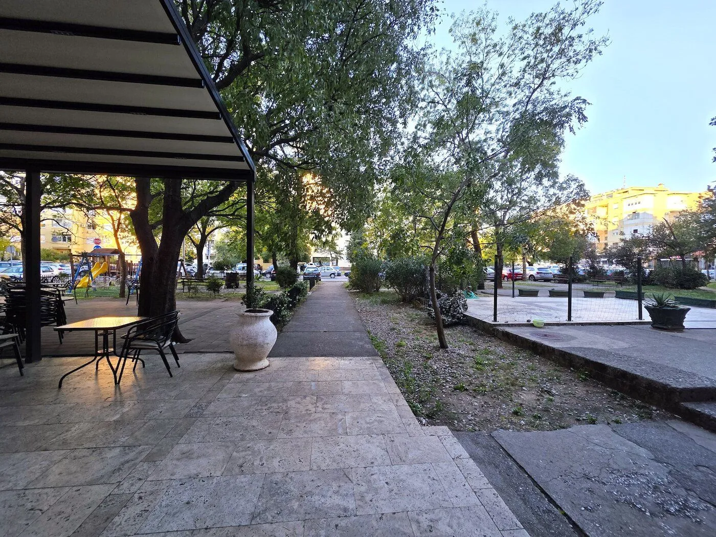 Natkrivena terasa sa stolom i stolicama ispred zgrade.