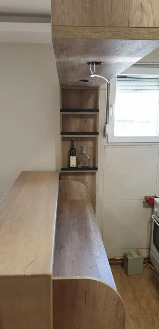 A wooden bar counter with built-in shelves next to a kitchen area.