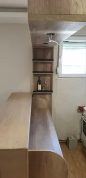 A wooden bar counter with built-in shelves next to a kitchen area. - image 19