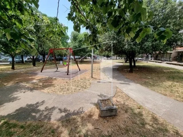 Dvorište sa igralištem i stazama ispred zgrade.