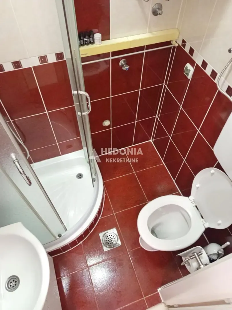 Kupatilo sa tuš kabinom i crvenim zidnim pločicama.