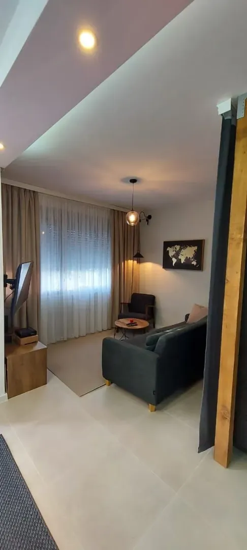 Dnevna soba sa garniturom, televizorom i prozorom sa zavjesama.