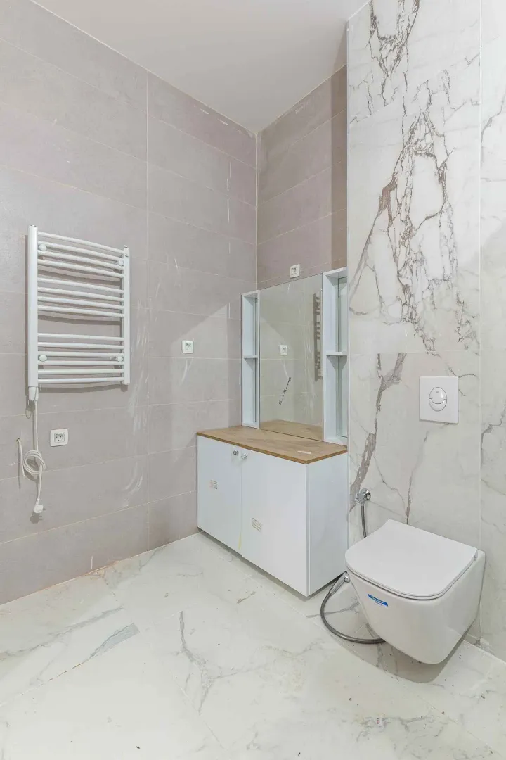 Moderne kupatilo sa pločicama u imitaciji mramora, WC šoljom i umivaonikom.