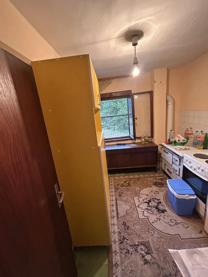 Jednostavna kuhinja sa šporetom, žutim ormarom i tepihom.