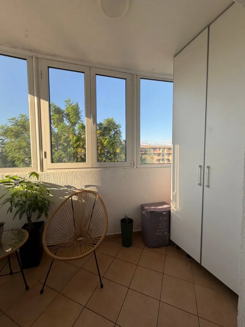 Zastakljena terasa sa garderoberom, stolicom i sobnim biljkama.