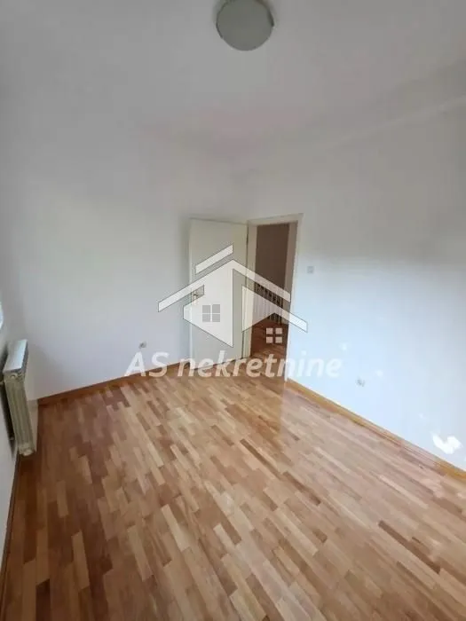 Prazna soba sa parketom i belim zidovima.