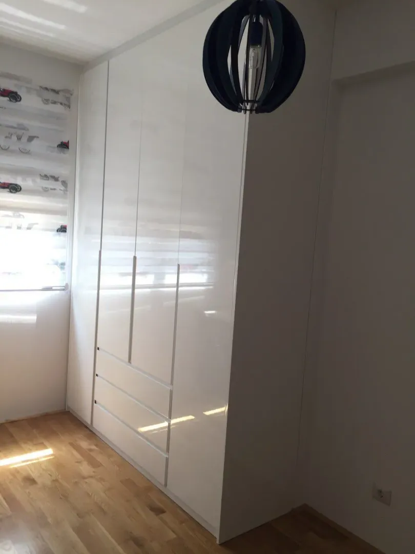 Built-in high-gloss white wardrobe in a room with wooden floors.
