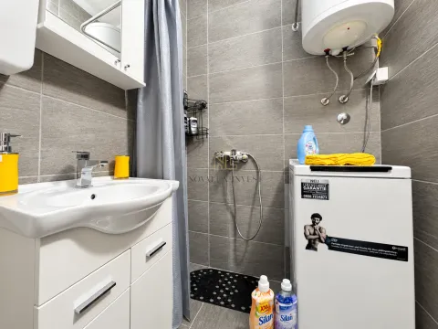Manje kupatilo obloženo sivim pločicama sa umivaonikom i veš mašinom. - image 10