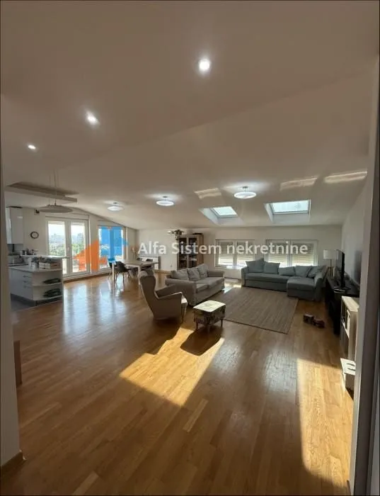 Spacious open-plan living room with wooden flooring, sofa set, and skylights.