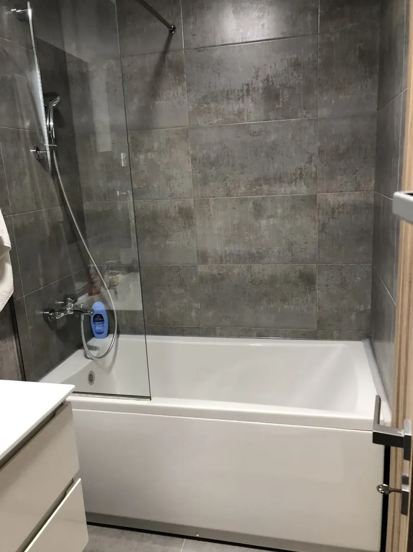 Modern bathroom with a bathtub and grey tiles.