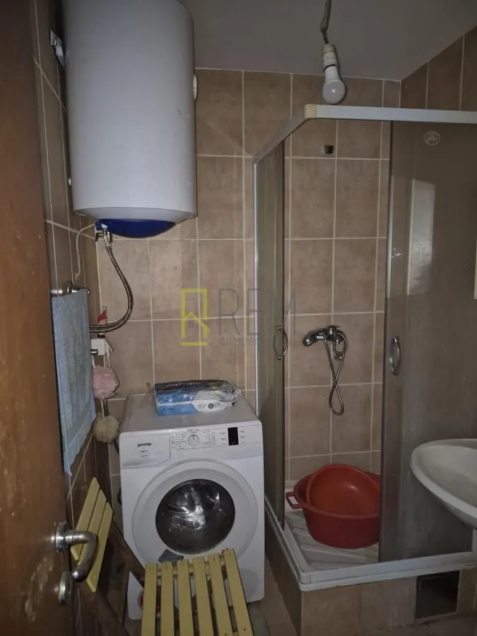 Manje opremljeno kupatilo sa tuš kabinom i veš mašinom.