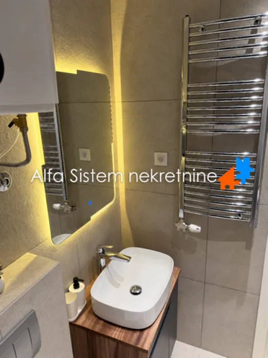 Smaller bathroom with a washbasin, backlit mirror, and a towel rail.