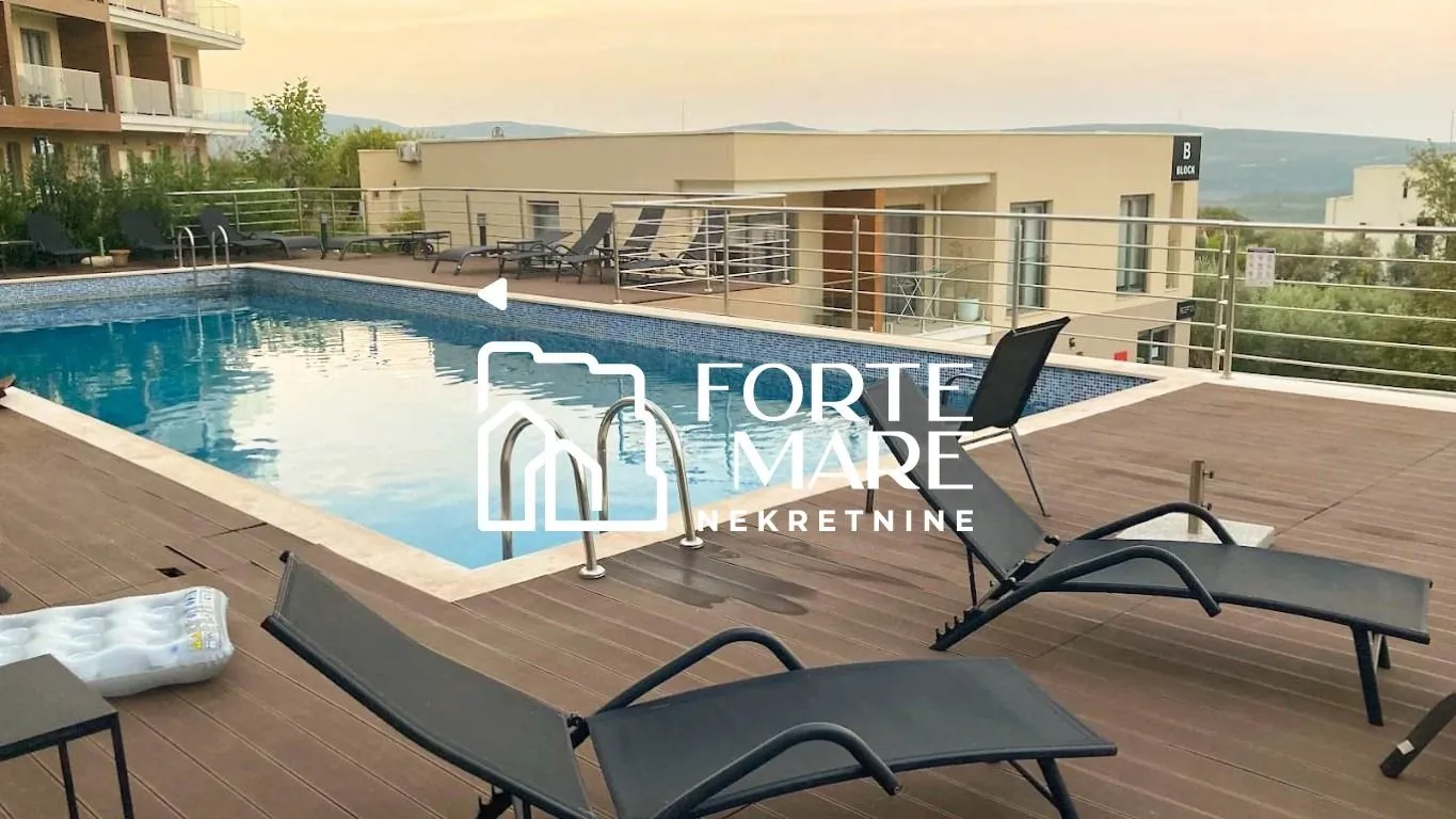 Bazen sa drvenom terasom za sunčanje i ležaljkama ispred stambenog objekta.