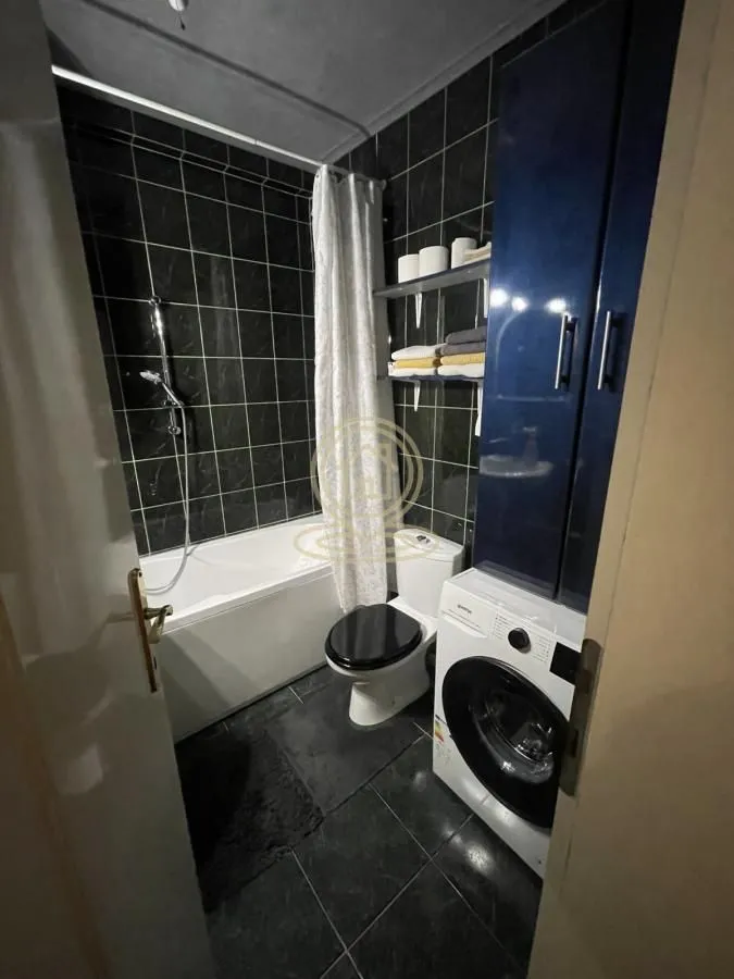Bathroom with dark tiles, bathtub, toilet, and washing machine.