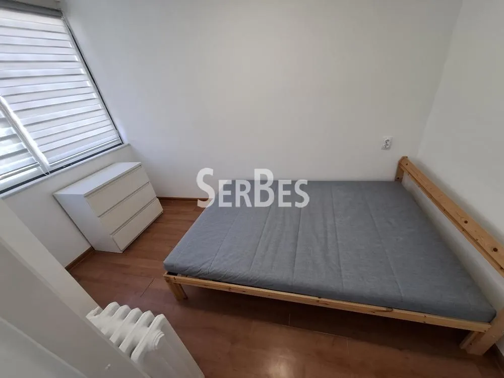 Manja spavaća soba sa drvenim krevetom i komodom.