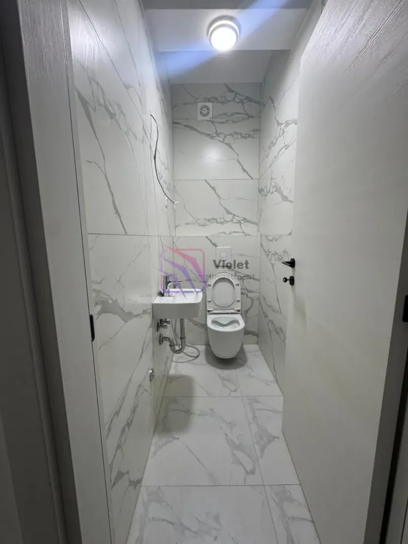 Manje kupatilo obloženo keramičkim pločicama sa efektom mermera.