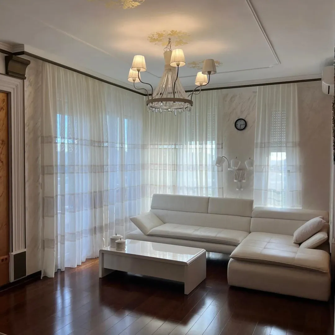 Living room with a white sectional sofa and large windows covered with curtains.