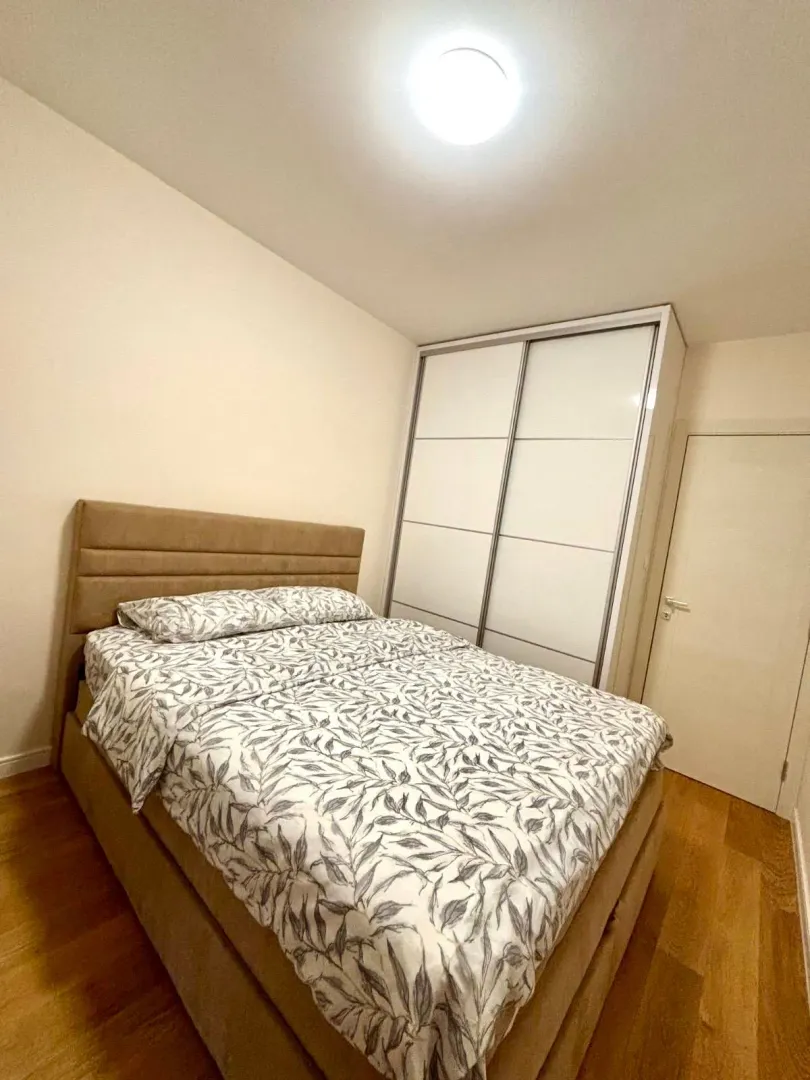 Spavaća soba sa bračnim krevetom, garderoberom i drvenim podom.