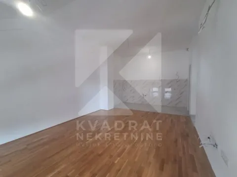 Empty room with wooden flooring and a designated kitchen area. - image 3