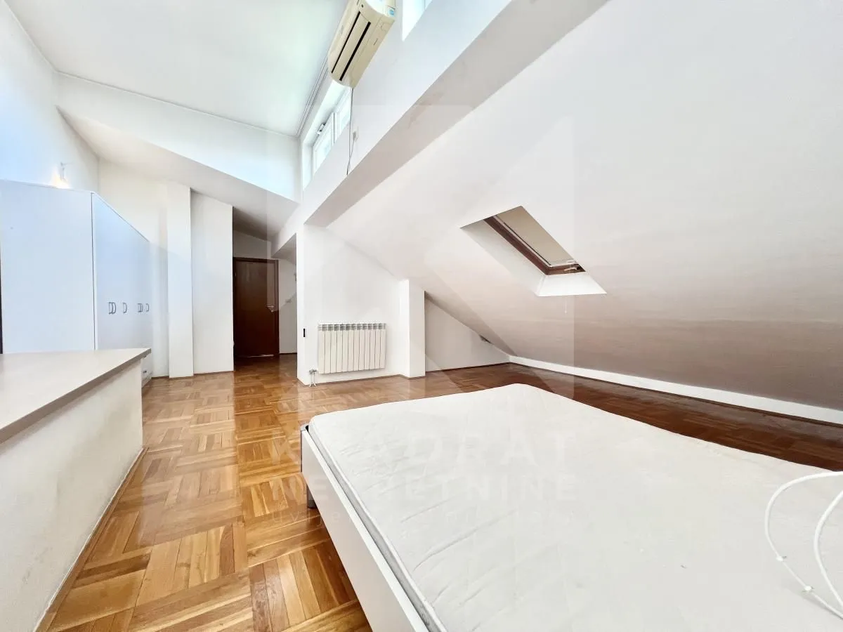 Attic bedroom with a bed, parquet flooring, and a skylight.