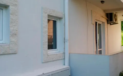 Pogled na bijelu fasadu zgrade sa prozorima i kamenim okvirom. - image 3