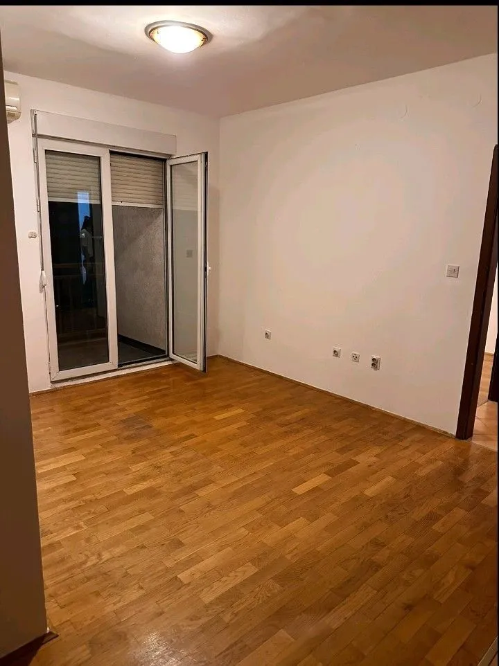 An empty room with wooden parquet flooring and balcony doors.
