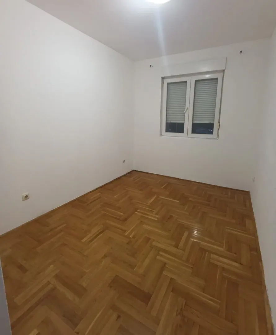 Prazna soba sa bijelim zidovima i drvenim parketom.
