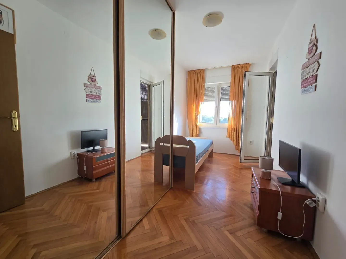 Small bedroom with a bed, parquet flooring, and a mirrored wardrobe.