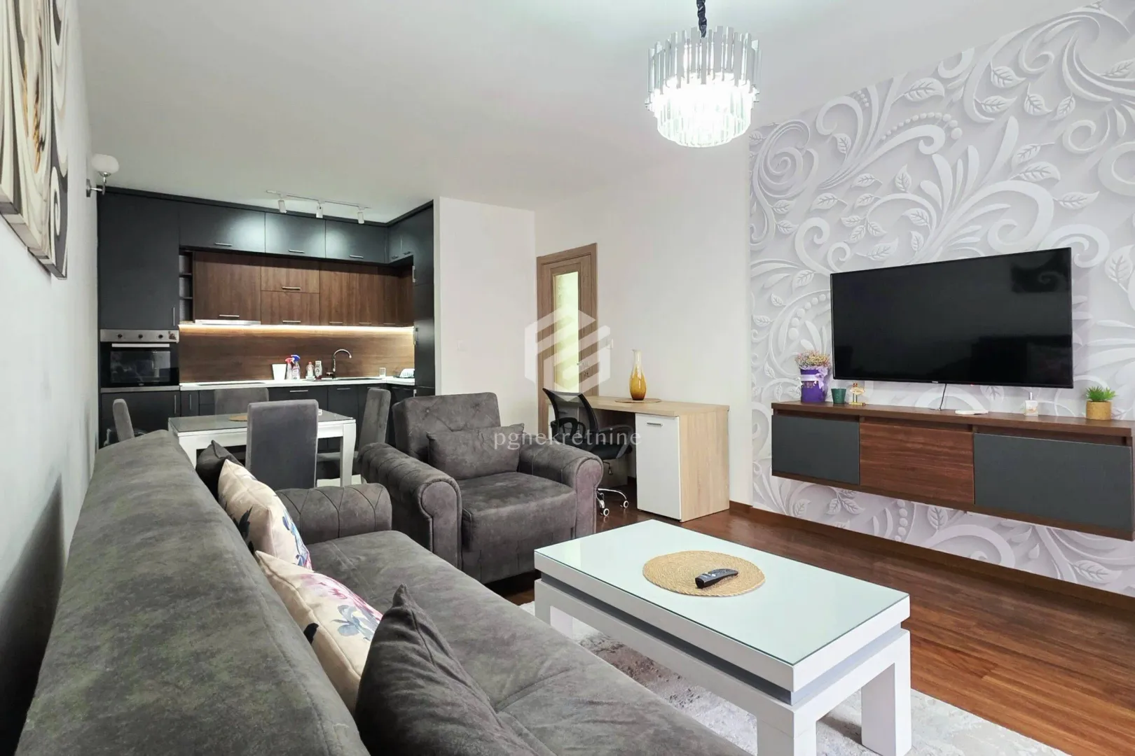 Living room with a sofa, TV, and kitchen in the background.