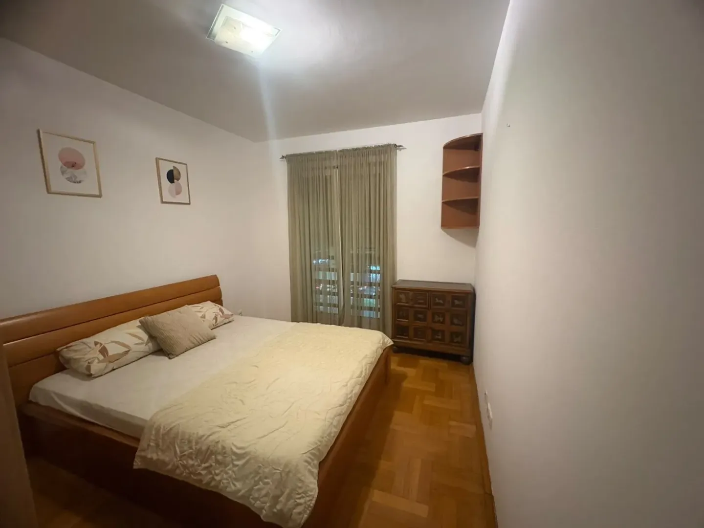 Furnished bedroom with a double bed, cabinet, and parquet flooring.