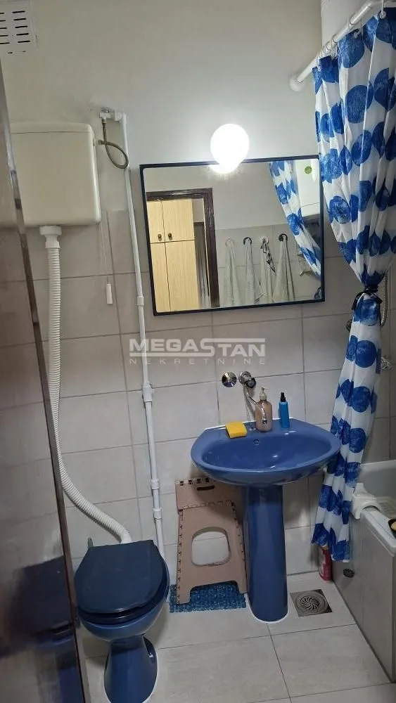 Manje kupatilo sa plavim umivaonikom, WC šoljom i kadom sa zavesom.