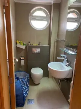 Small bathroom with a toilet, washbasin, and round window. - image 10