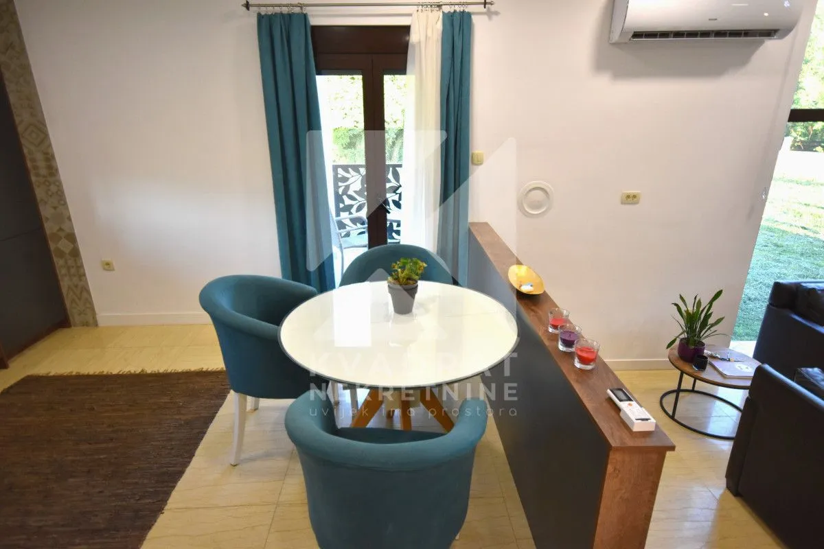 Dining area with a round table and blue armchairs next to balcony doors.